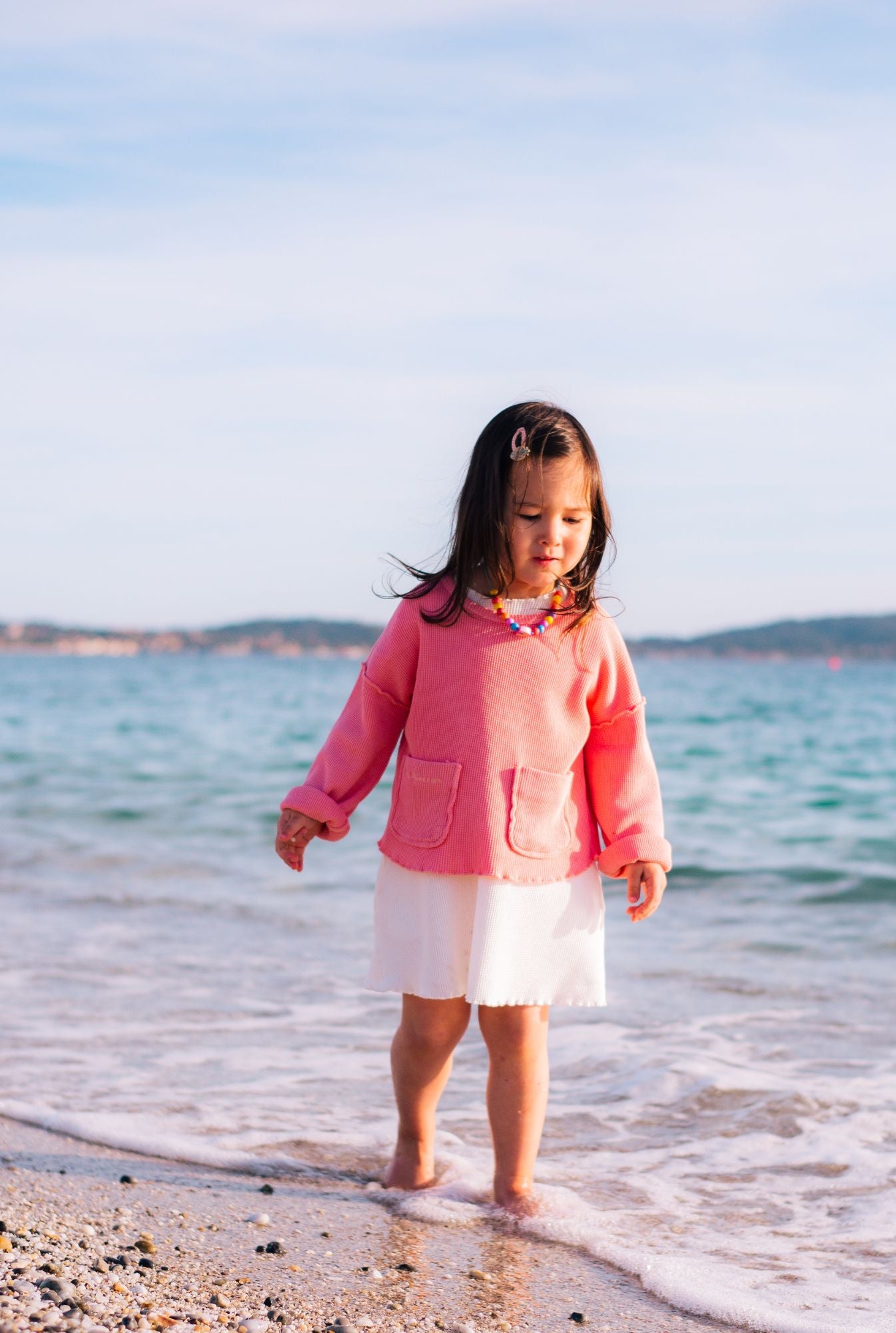 Everyday play in comfortable and organic kids clothes. 3 years old girl in her pink top and white dress. Made from organic cotton waffle.