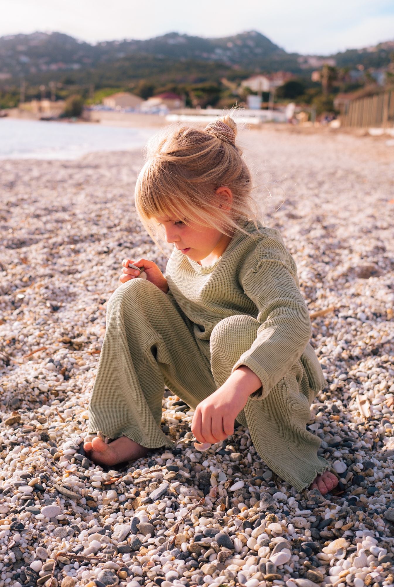 A girl by the beach collecting sea shells in her comfy green set by Tiny Advocates. Made from organic cotton, it is stylish yet comfortable.