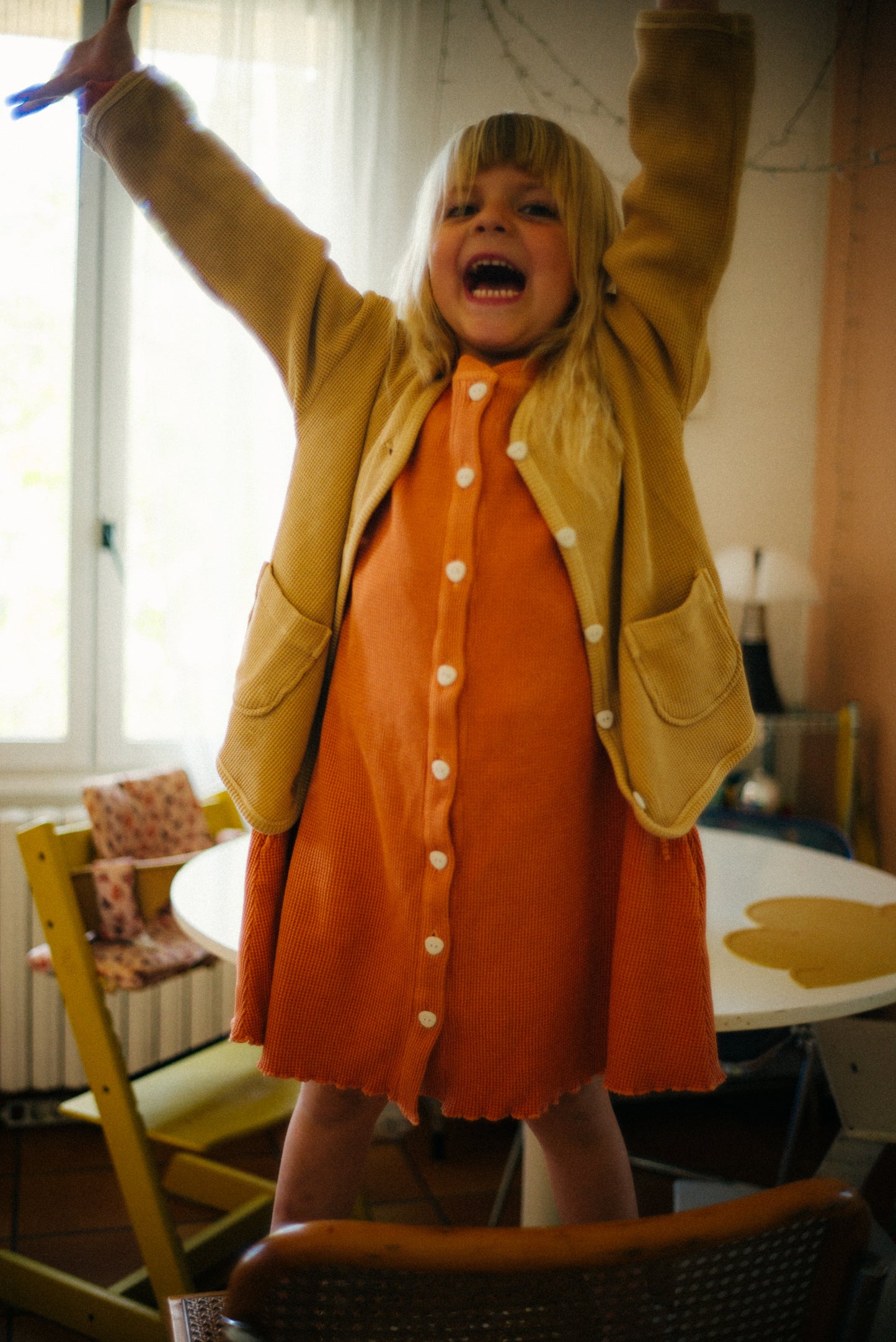 a girl is wearing a comfortable sienna long sleeve dress and a sandstone cardigan on top. Both pieces are made with 100% organic cotton and garment dyed in natural minerals. Fabric is breathable and perfect for indoor and outdoor play.