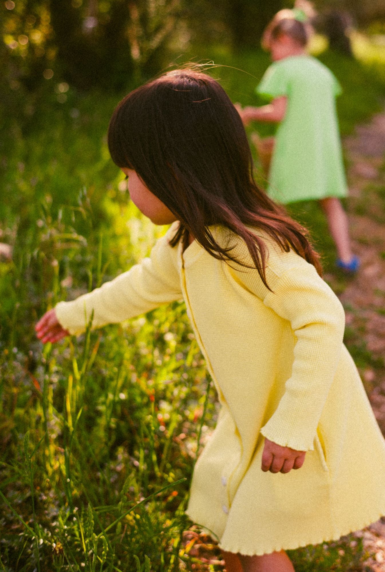 A three years old girl wearing a beautiful yellow dress and playing the field with flowers. Dress is made with 100% organic cotton waffle fabric that is breathable and perfect for all year round.
