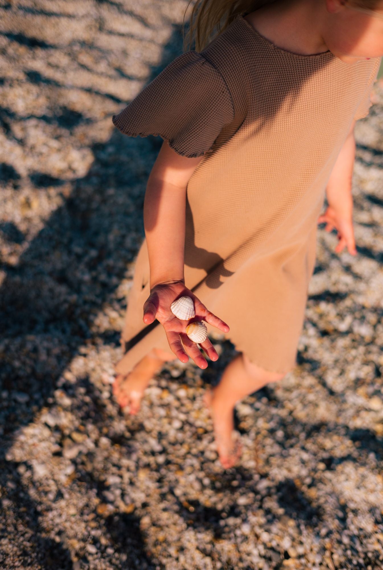 6 years old girl playing with sea shells. She is wearing a comfortable and stylish dress made from organic cotton.