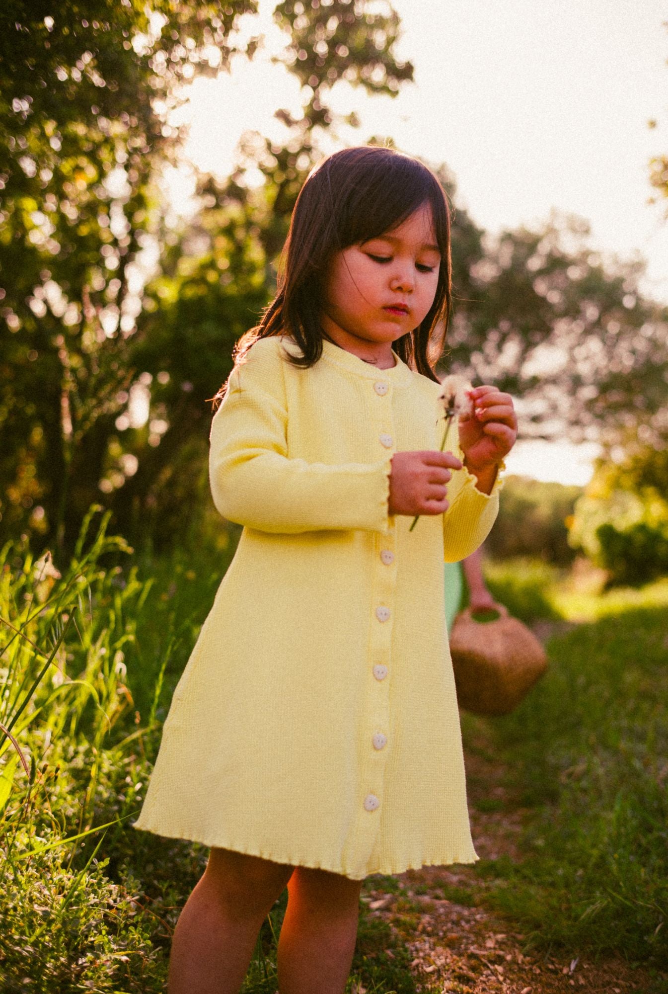 A little girl is wearing a comfortable yellow dress with pockets and buttons. The dress is made with breathable 100% organic cotton waffle fabric and garment dyed with natural minerals.