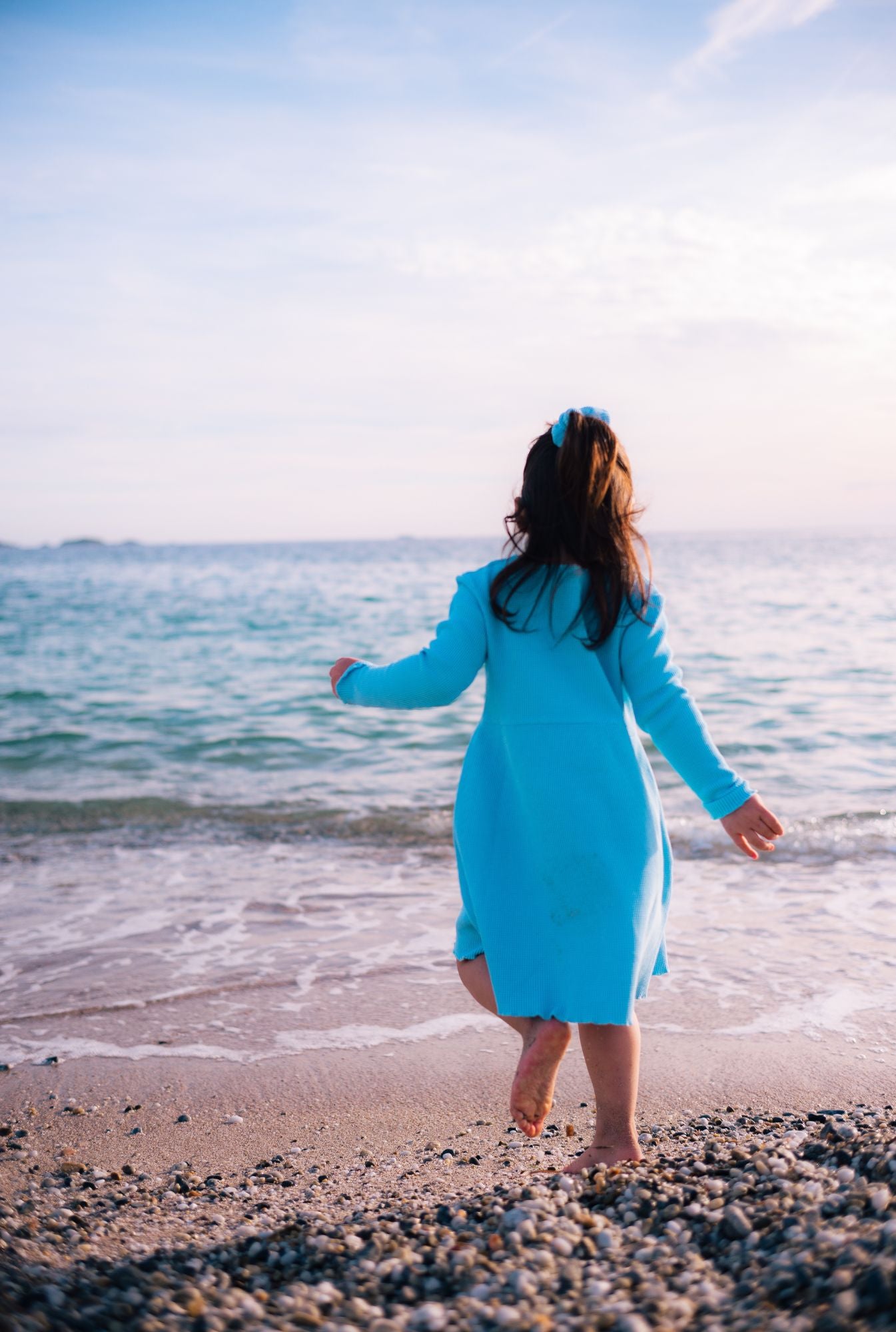 A little girl playing by the beach and wearing a long sleeve comfortable dress. It's made from 100% organic cotton dress and garment dyed in natural minerals.