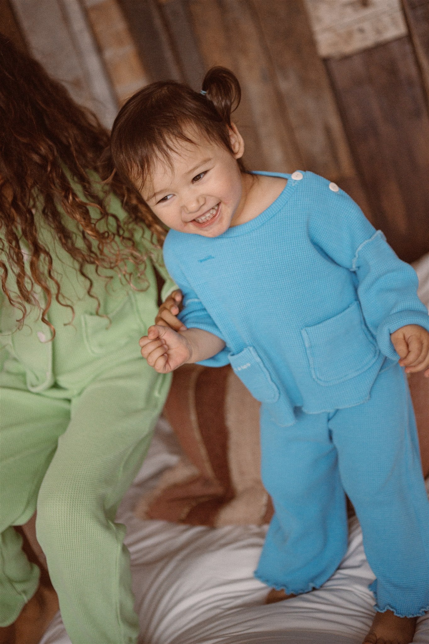 Two girls jumping on bed in their cozy organic waffle sets in stunning blue and green colors.