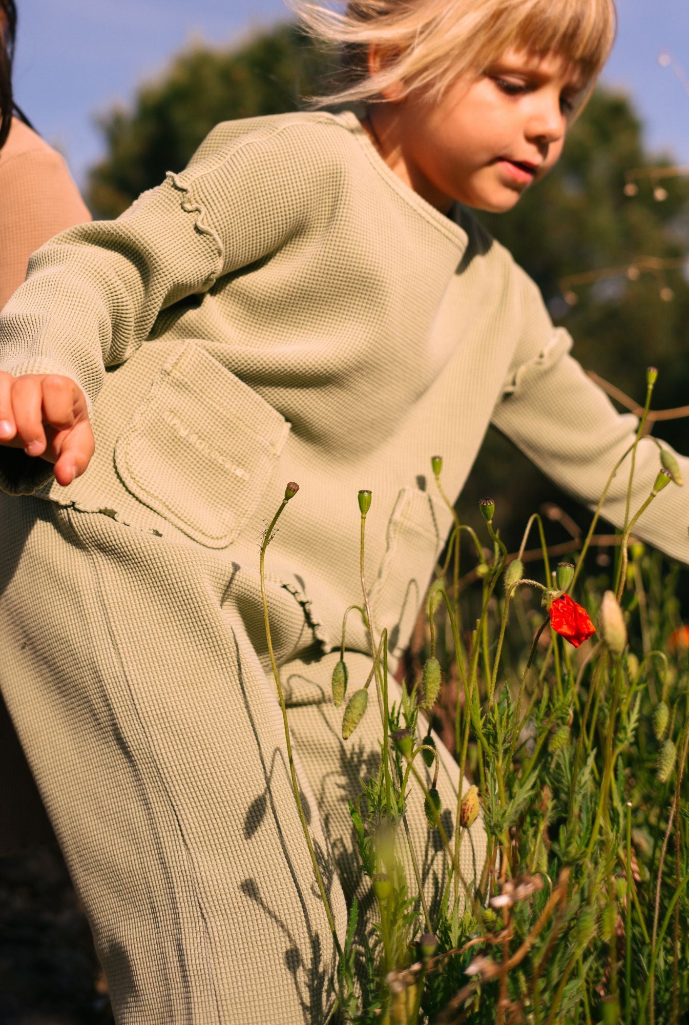 A 6 years old girl picking flowers in her comfortable and stylish set made by Tiny Advocates. Top and pants made from organic cotton and garment dyed with natural minerals.