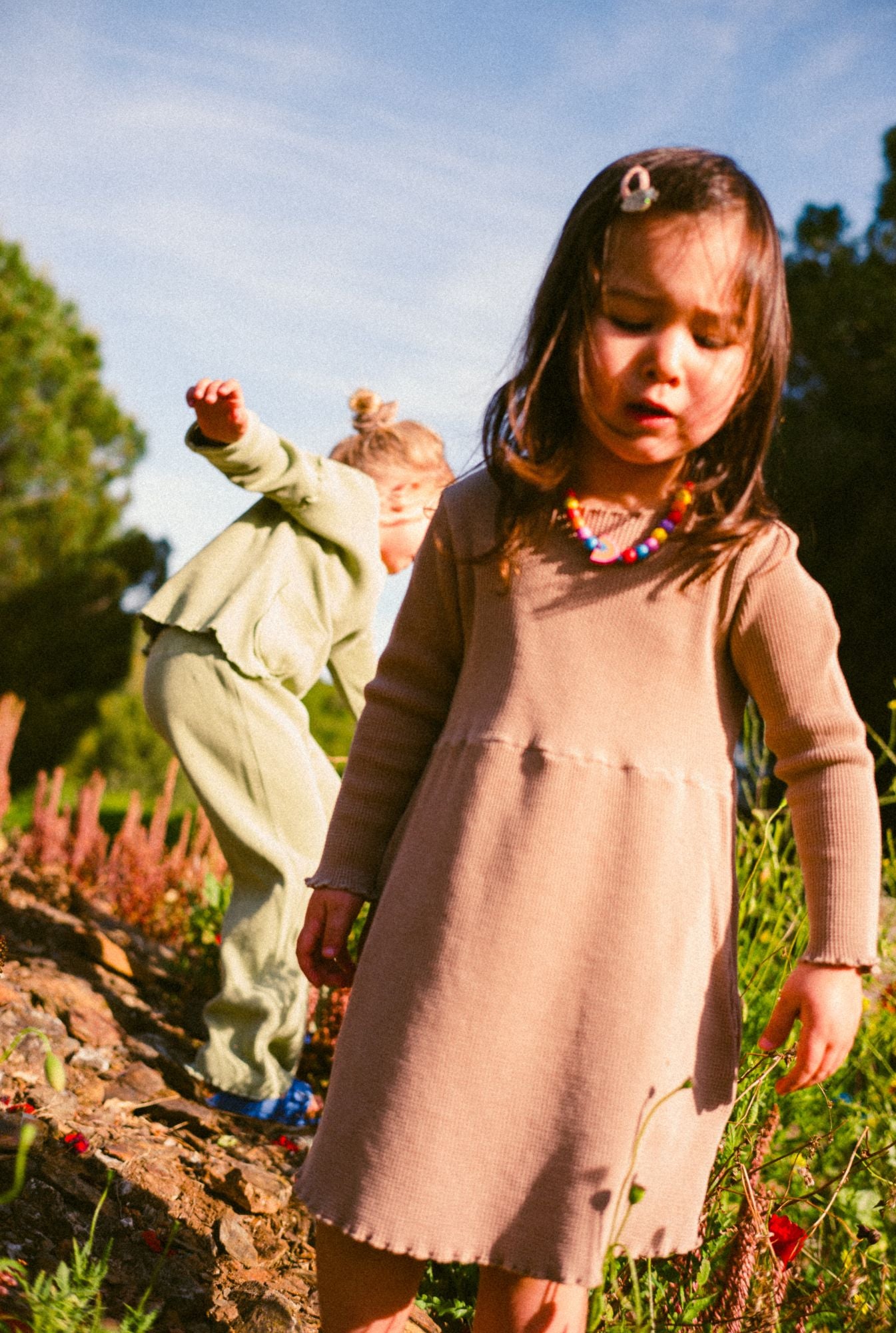 A little girl playing in the field and wearing buttery soft organic cotton waffle dress in ochre.