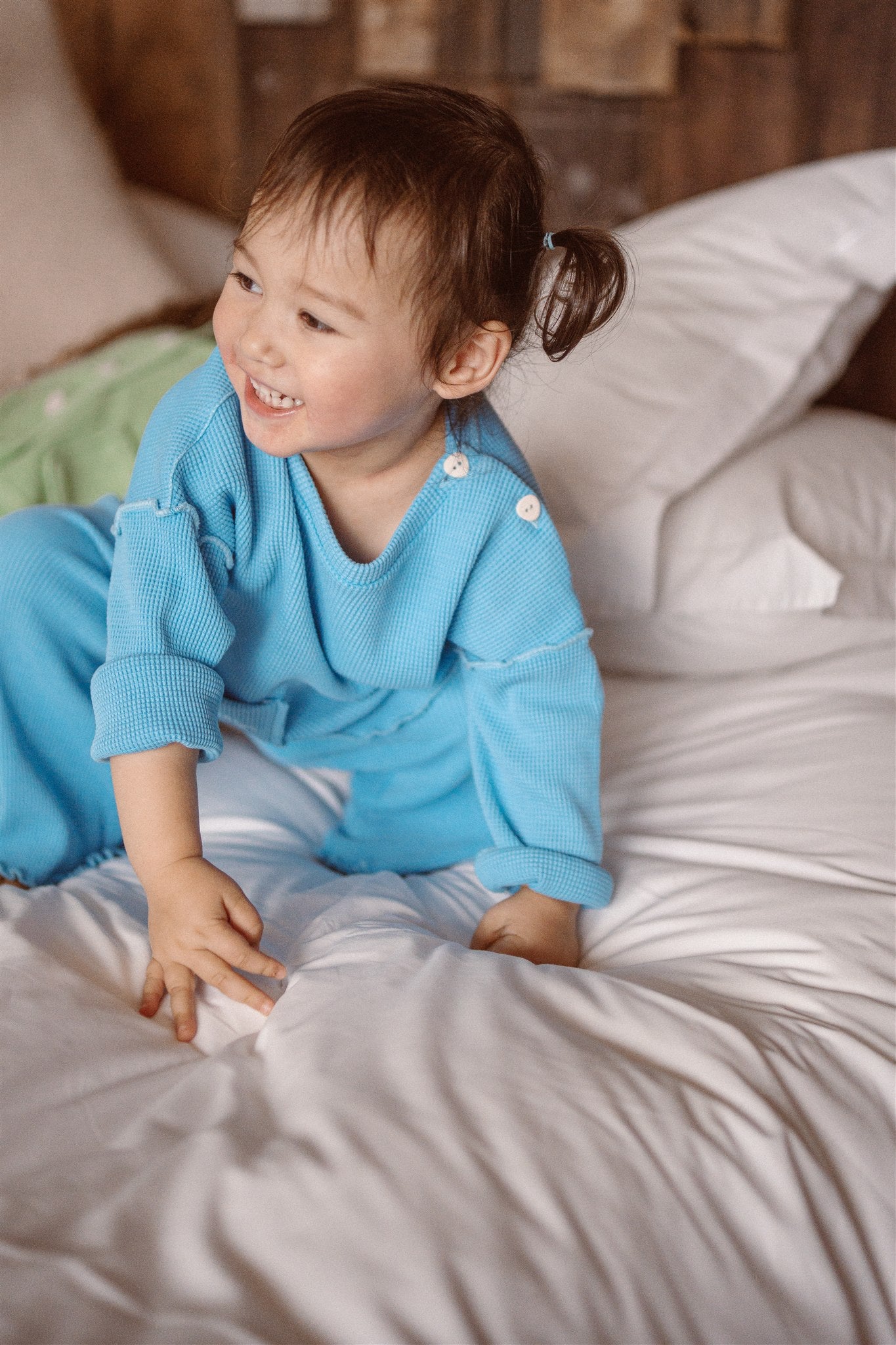 A little girl playing on a bed and wearing a beautiful sky blue top and pants. This eco-friendly kids wear made from 100% organic cotton and garment dyed with natural minerals.
