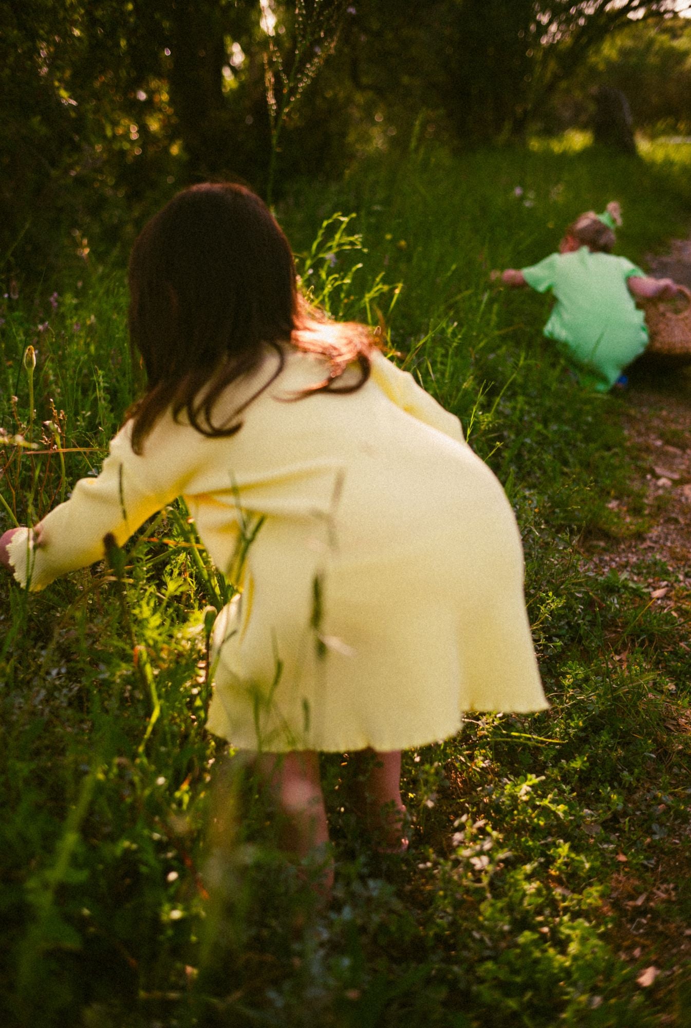 A three years old girl wearing a yellow dress with buttons and pockets. She is playing in the field in the most comfortable everyday dress. Made with 100% organic cotton waffle fabric.