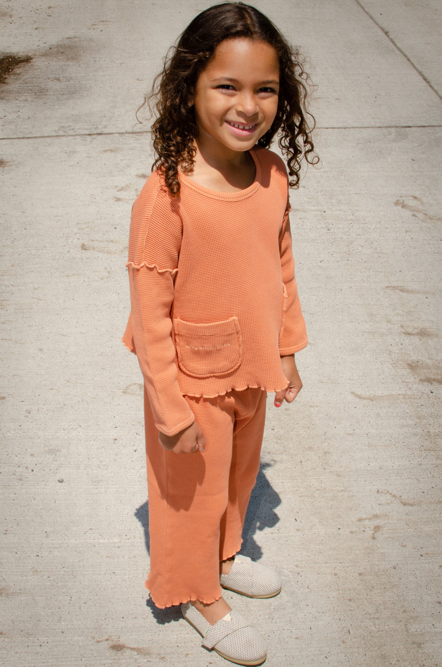 A 5 years old girl dressed in the comfortable organic cotton waffle sweater and pants in sienna.