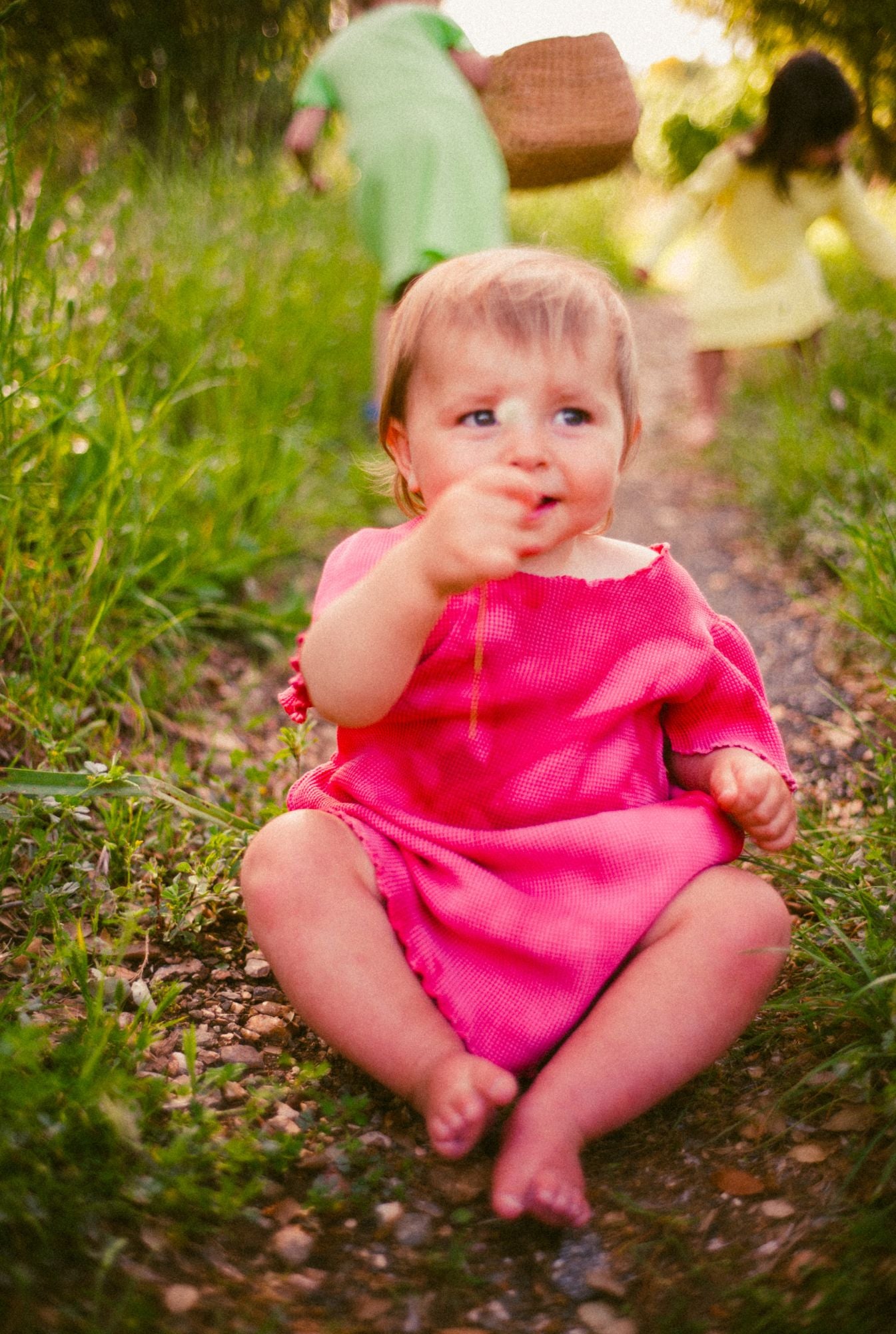 1 year old girl is playing with flowers and wearing a beautiful, comfortable, and colorful dress in pink tie dye. The dress is made by Tiny Advocates. It comes in a variety of beautiful colors, has side pockets, and beautiful details around the neckline and sleeves.