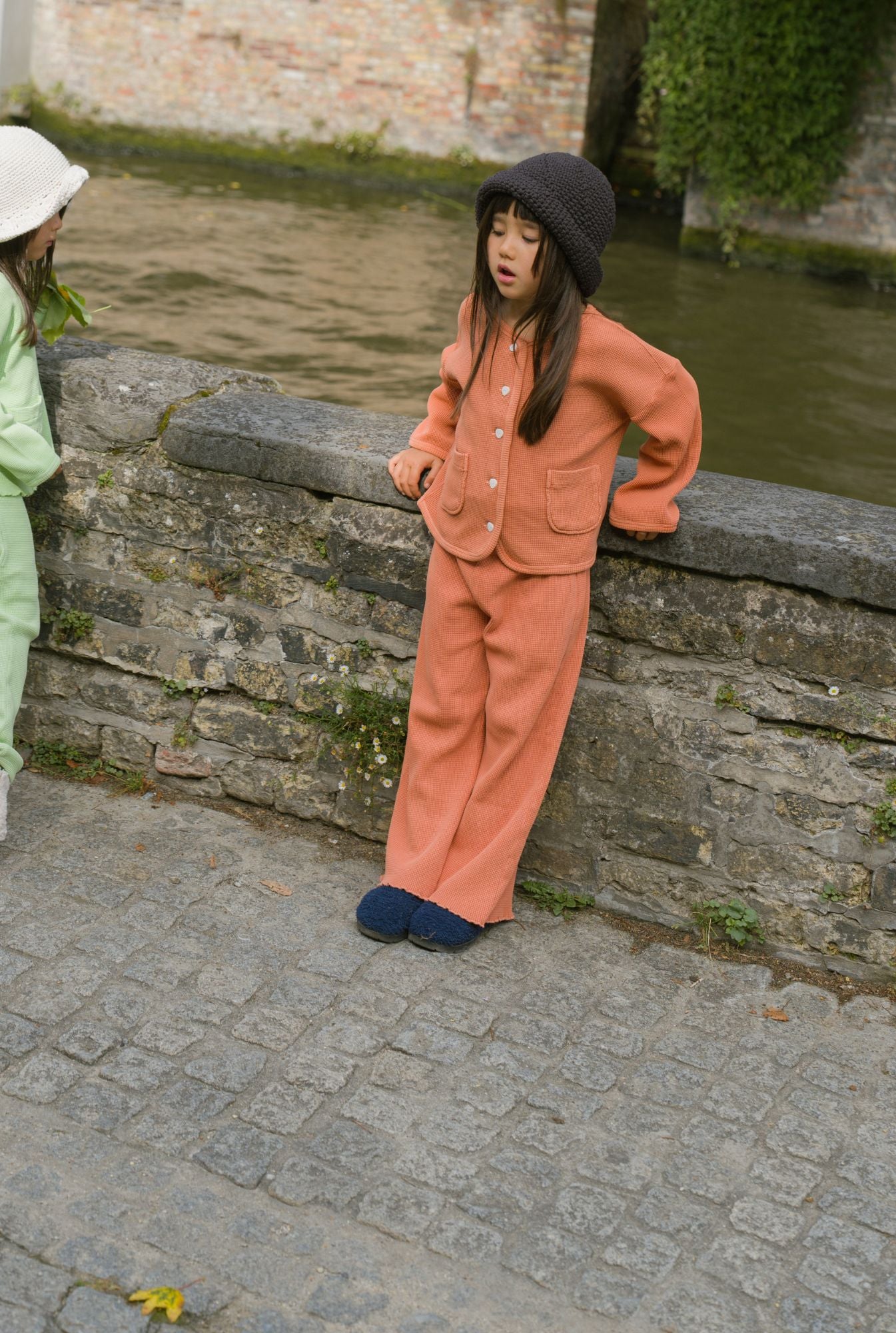 Two girls standing by the river and wearing comfortable sets by Tiny Advocates. Older girl is wearing sienna pants and cardigan and younger one is wearing a light green top with pants. Made from organic cotton waffle fabric that is breathable and soft.