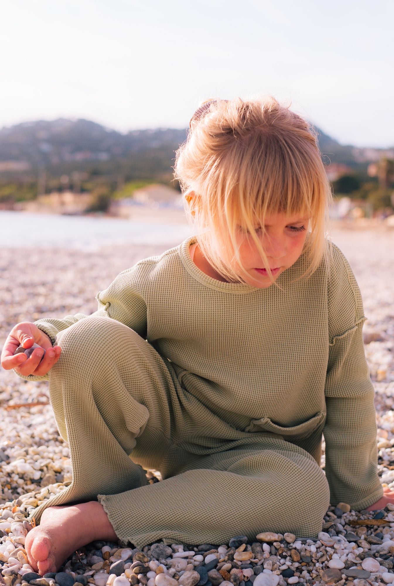 A girl by the beach collecting sea shells in her comfy green set by Tiny Advocates. Made from organic cotton, it is stylish yet comfortable.