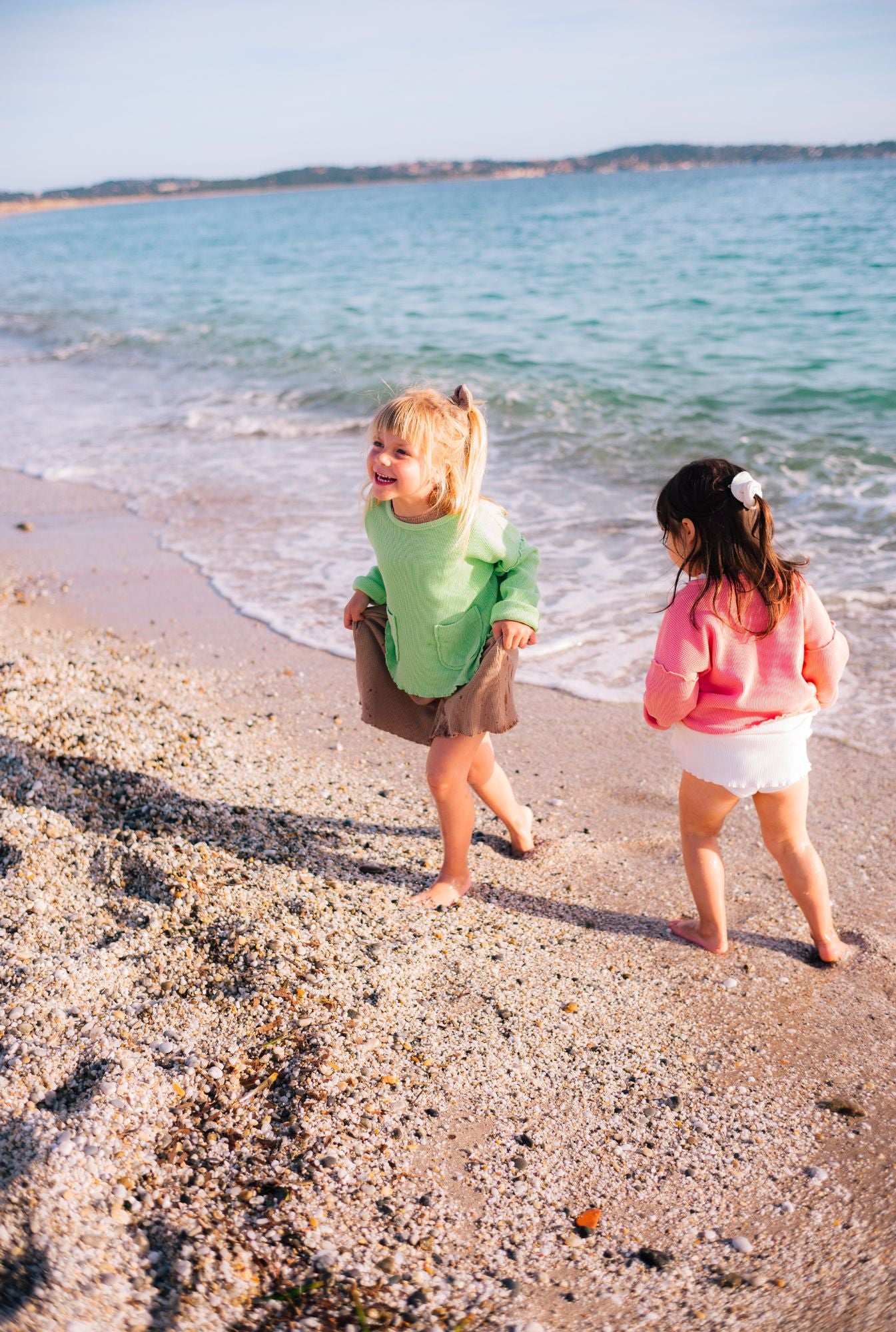Two girls wearing organic kids clothes by Tiny Advocates. Light green and pink sweaters with pockets.