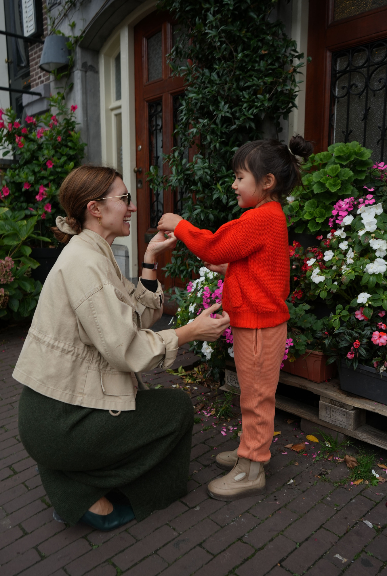 Woman and child interacting outdoors with flowers and a building in the background