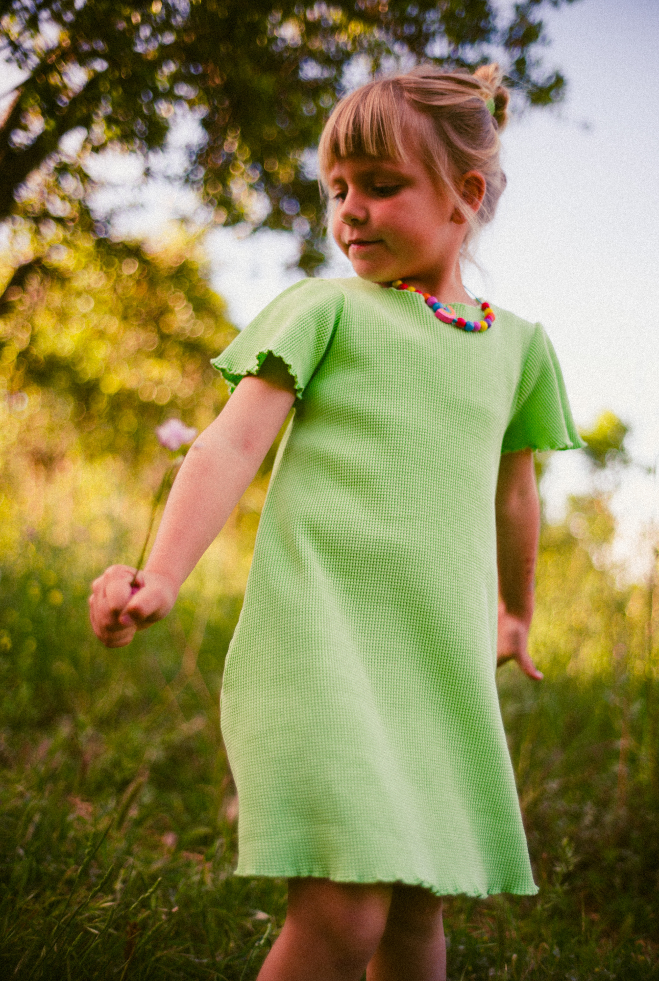 A little girl playing in the field in South of France. She is wearing a beautiful light green dress made from 100% organic cotton. The dress is soft, comfortable and comes with side pockets.