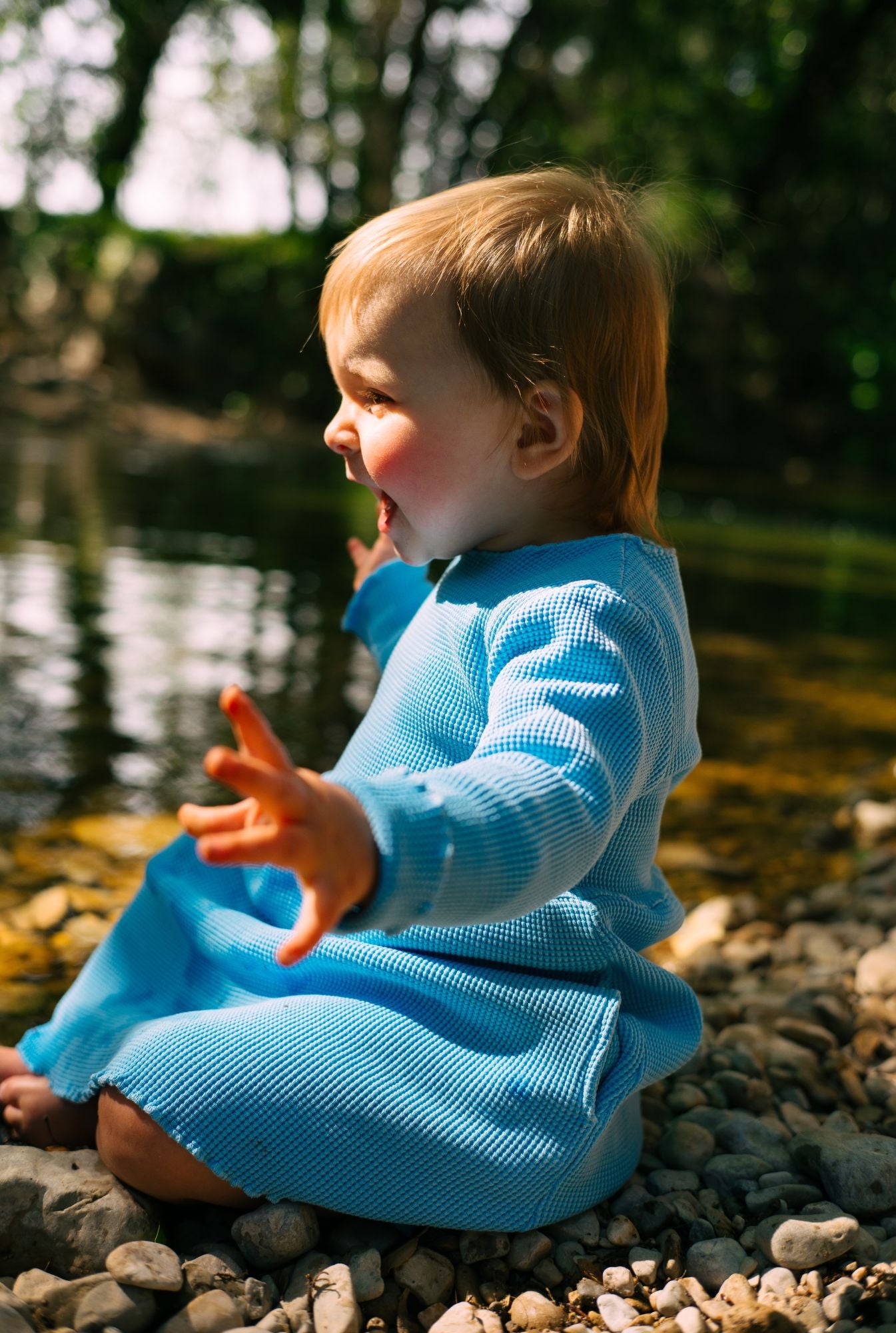 A toddler girl is wearing a long sleeve blue dress by the river in South of France. The dress is long sleeves and comes with lovely pockets. It is comfortable, breathable, and affordable.