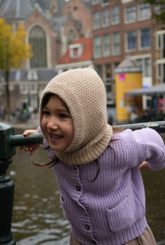 Child wearing a knitted  baby alpaca winter hat and purple 100% tanguis cotton sweater by a canal with buildings in the background