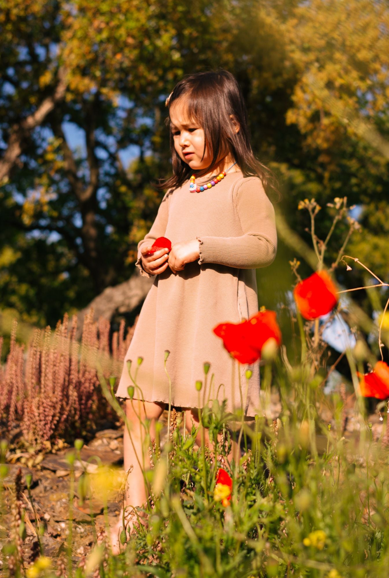 3 years old playing in the field and wearing breathable, organic cotton long sleeve dress in ochre.