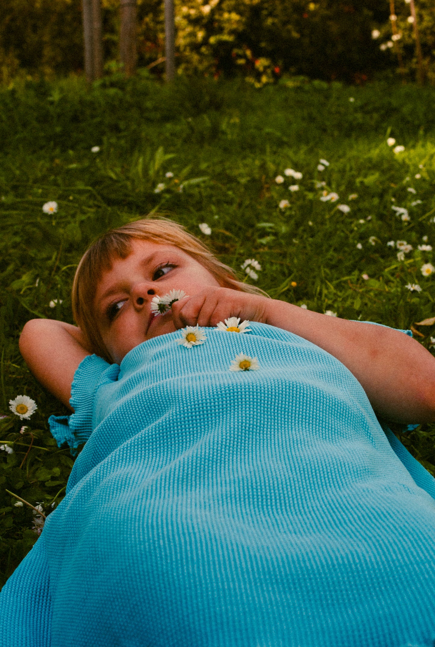 A little girl in the field playing with flowers. She is wearing a beautiful blue summer dress made from 100% organic cotton.