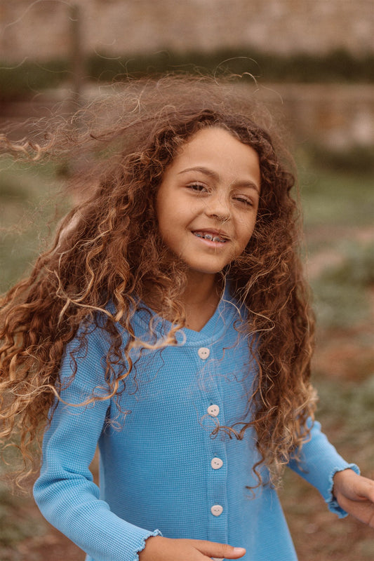 6 year old girl wearing a blue dress with pockets and buttons in buttery soft 100% organic cotton waffle blue color.