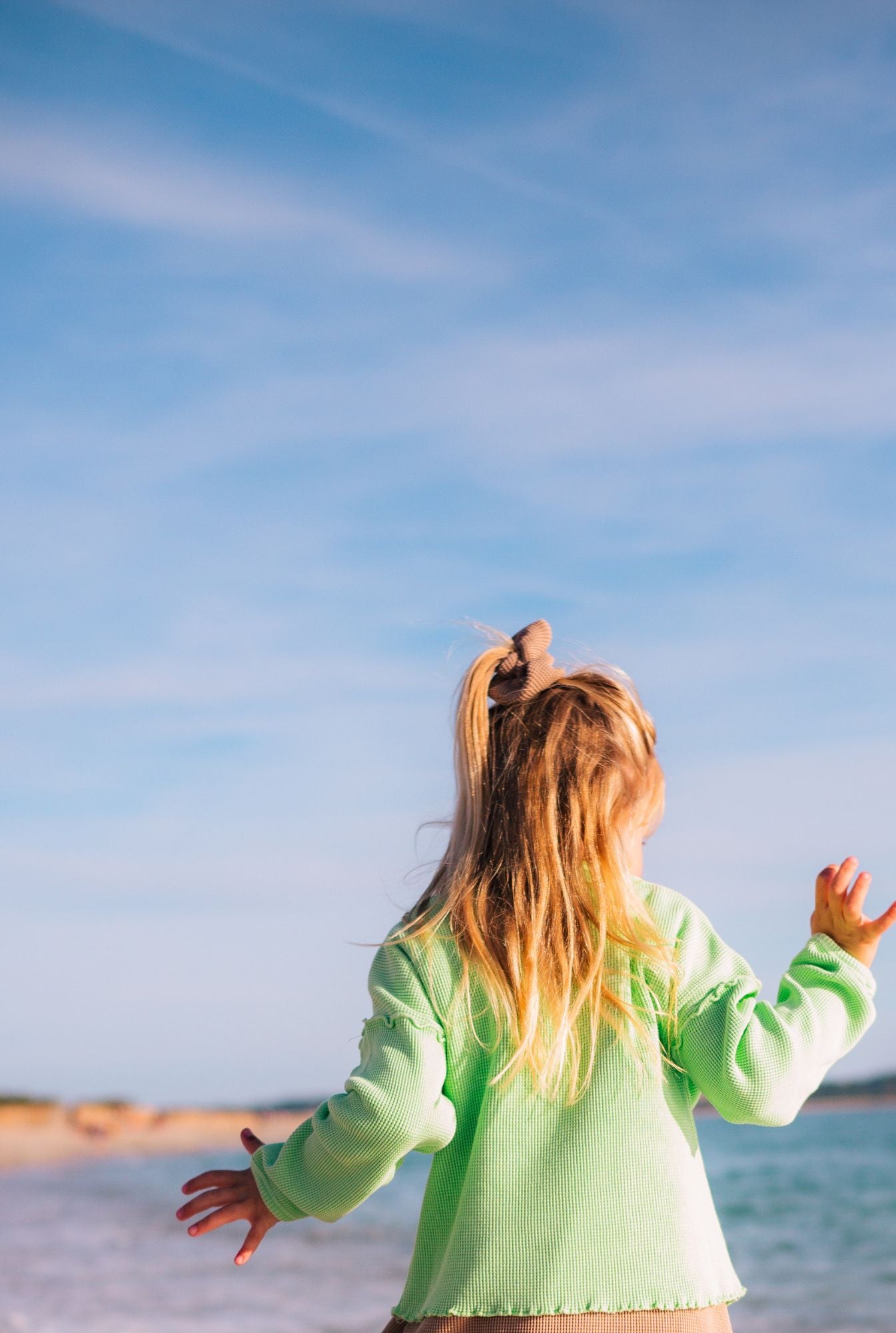 A little girl in the light green long sleeve top by the beach.