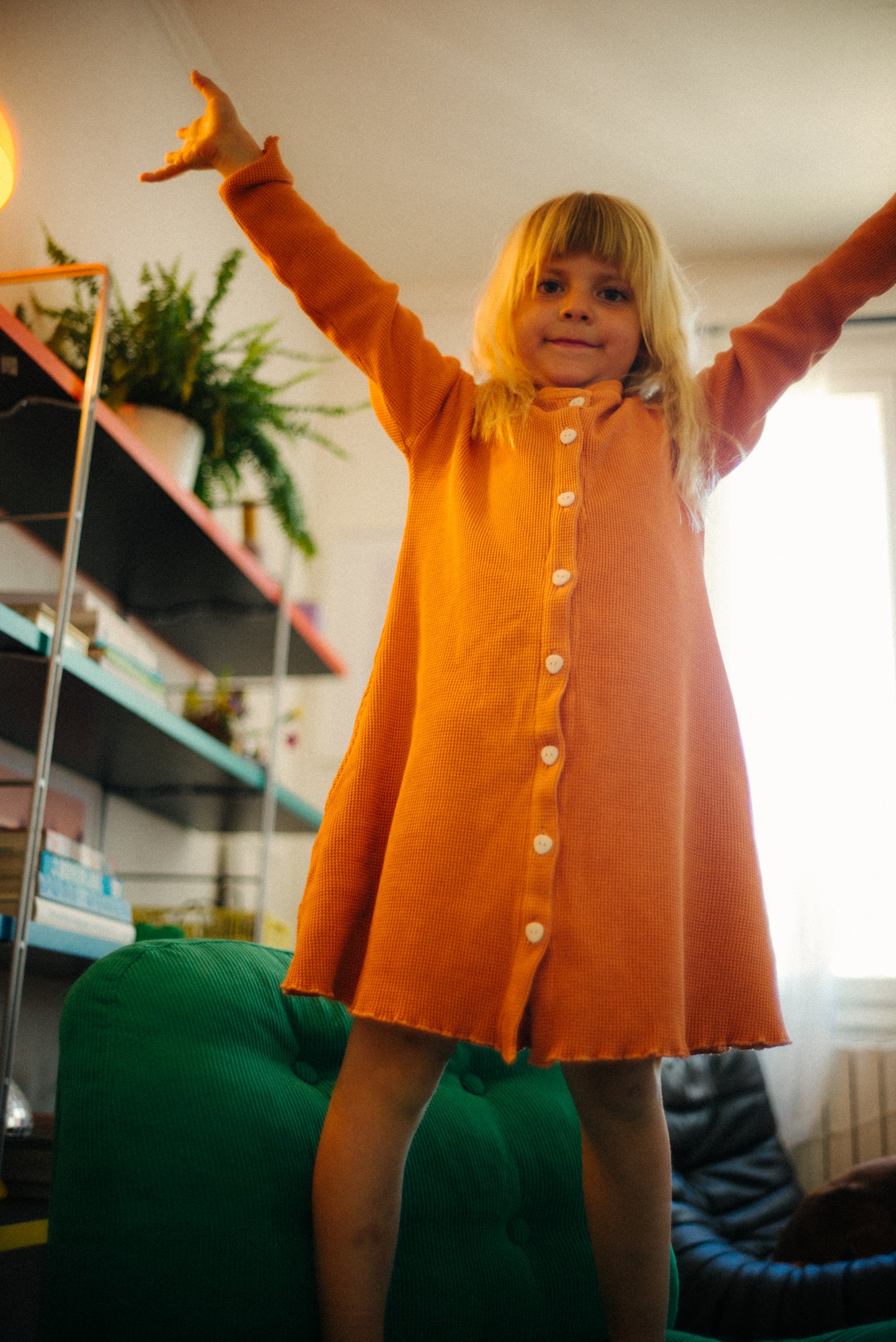 a girl is playing at home in her long sleeve dress with pockets and eco friendly buttons. It is made with 100% organic cotton waffle fabric and garment dyed in natural minerals. Perfect for at home and outdoor adventures.