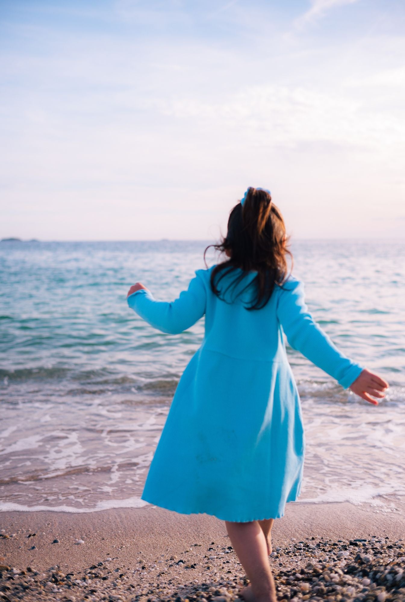 A little girl playing by the beach and wearing a long sleeve comfortable dress. It's made from 100% organic cotton dress and garment dyed in natural minerals.