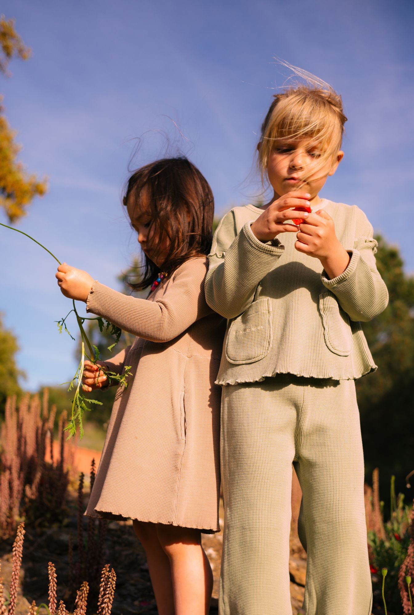 Two little girls picking flowers in their stylish and cozy clothes. Made from organic cotton in Portugal.