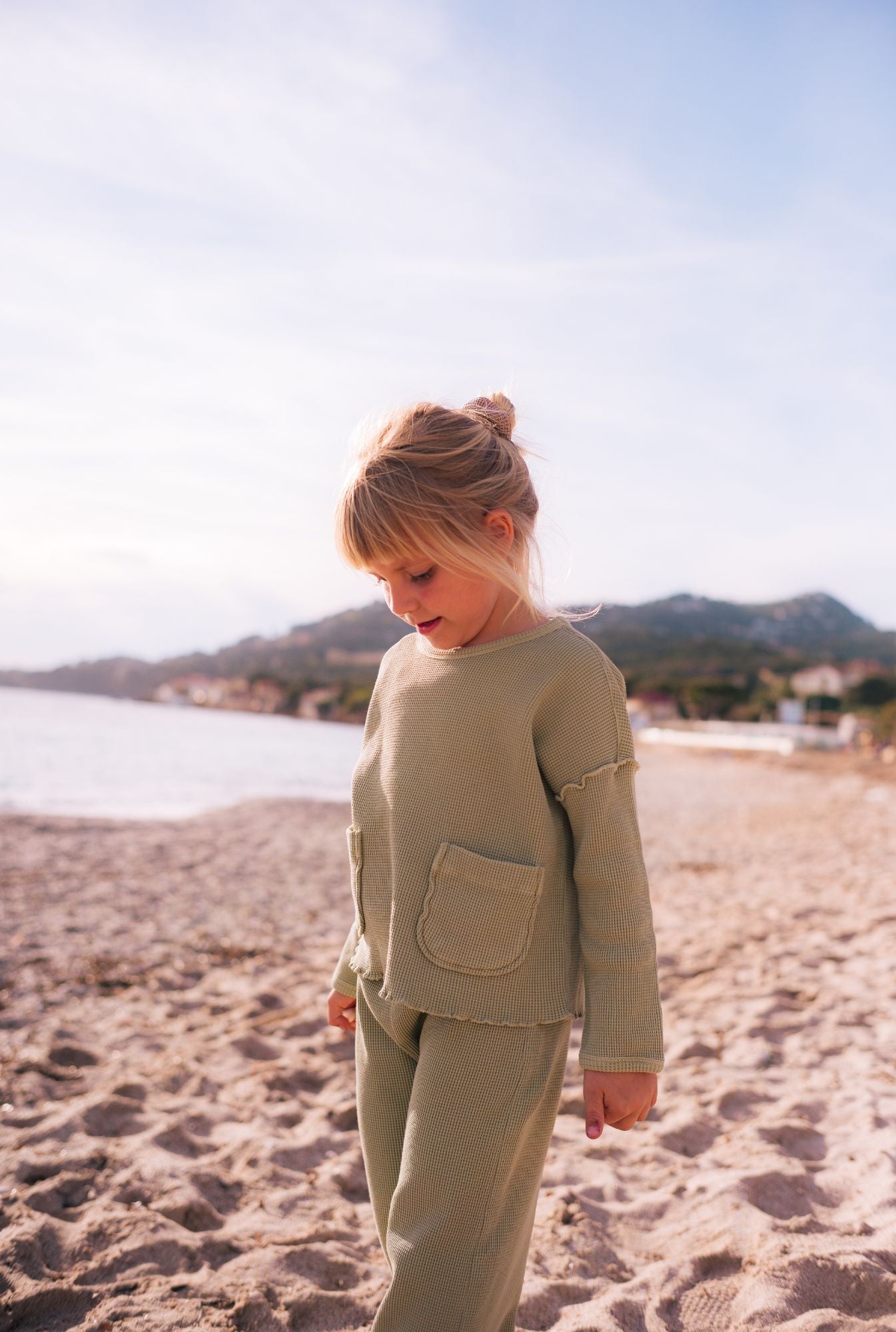 A little girl on the beach wearing an organic cotton set (pants and long sleeve top). 