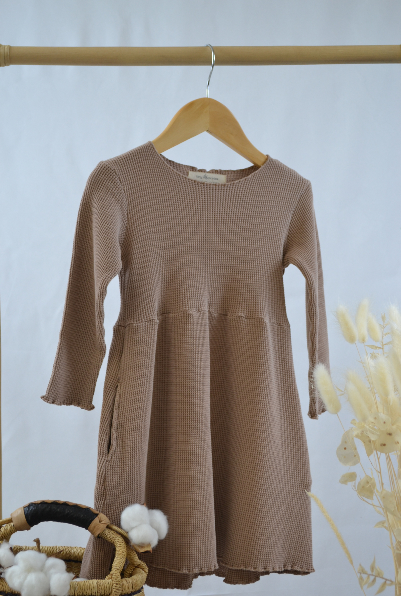 An image of a kids organic cotton long sleeve dress. The dress features empire waste, lettuce hem sleeve and neck finish, and comes with functional side pockets. Its comfortable, breathable and super cute.