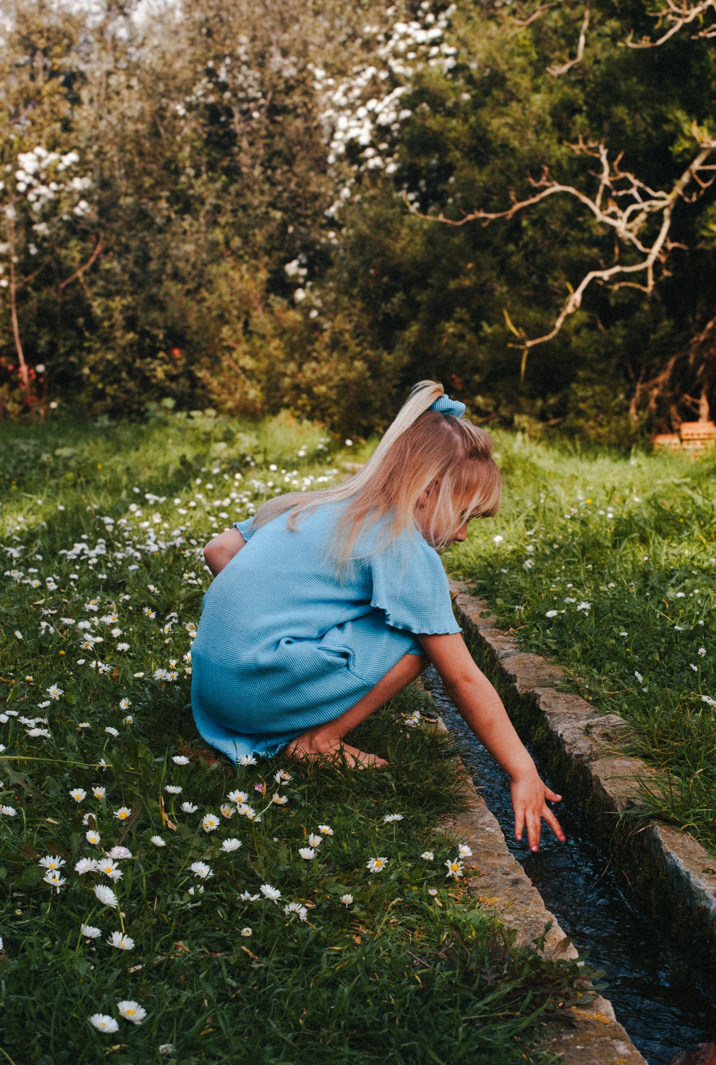 A little girl is wearing a blue dress made of organic cotton and garment dyed with natural minerals. She is playing in the field and enjoying summer.