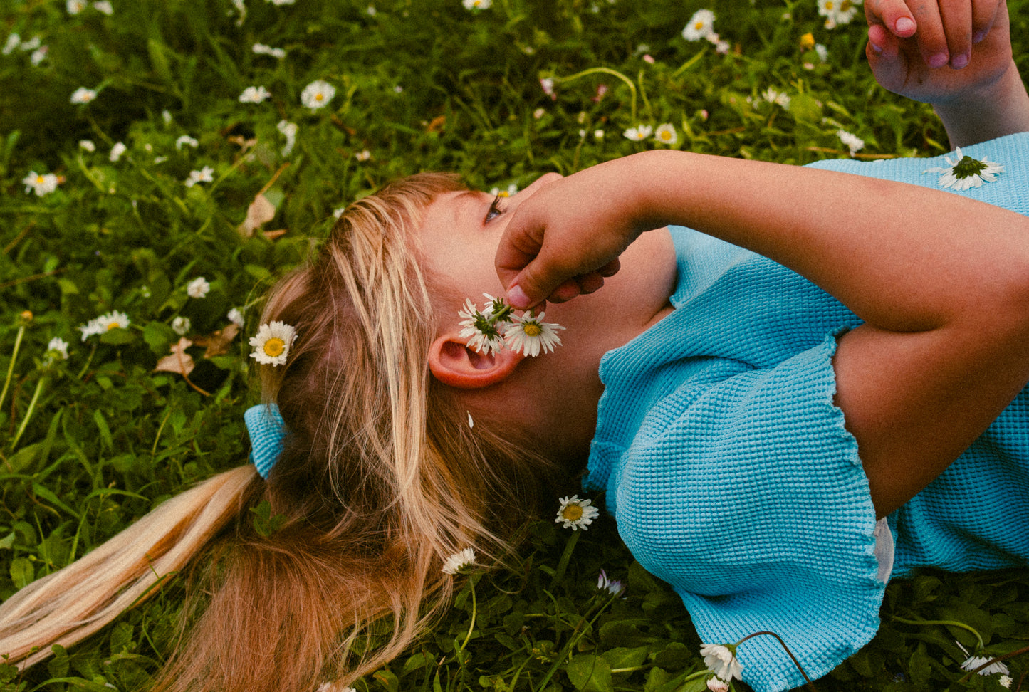 A little girl in the field playing with flowers. She is wearing a beautiful blue summer dress made from 100% organic cotton.