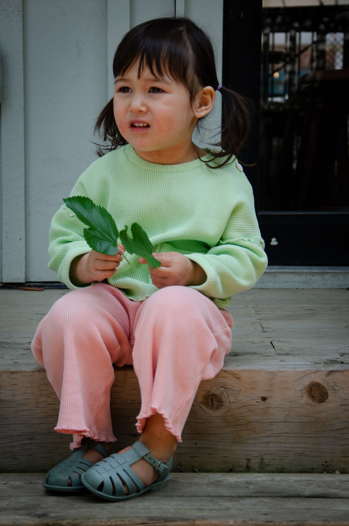 Little girl on the staircase wearing a light green organic long sleeve top and pink pants.