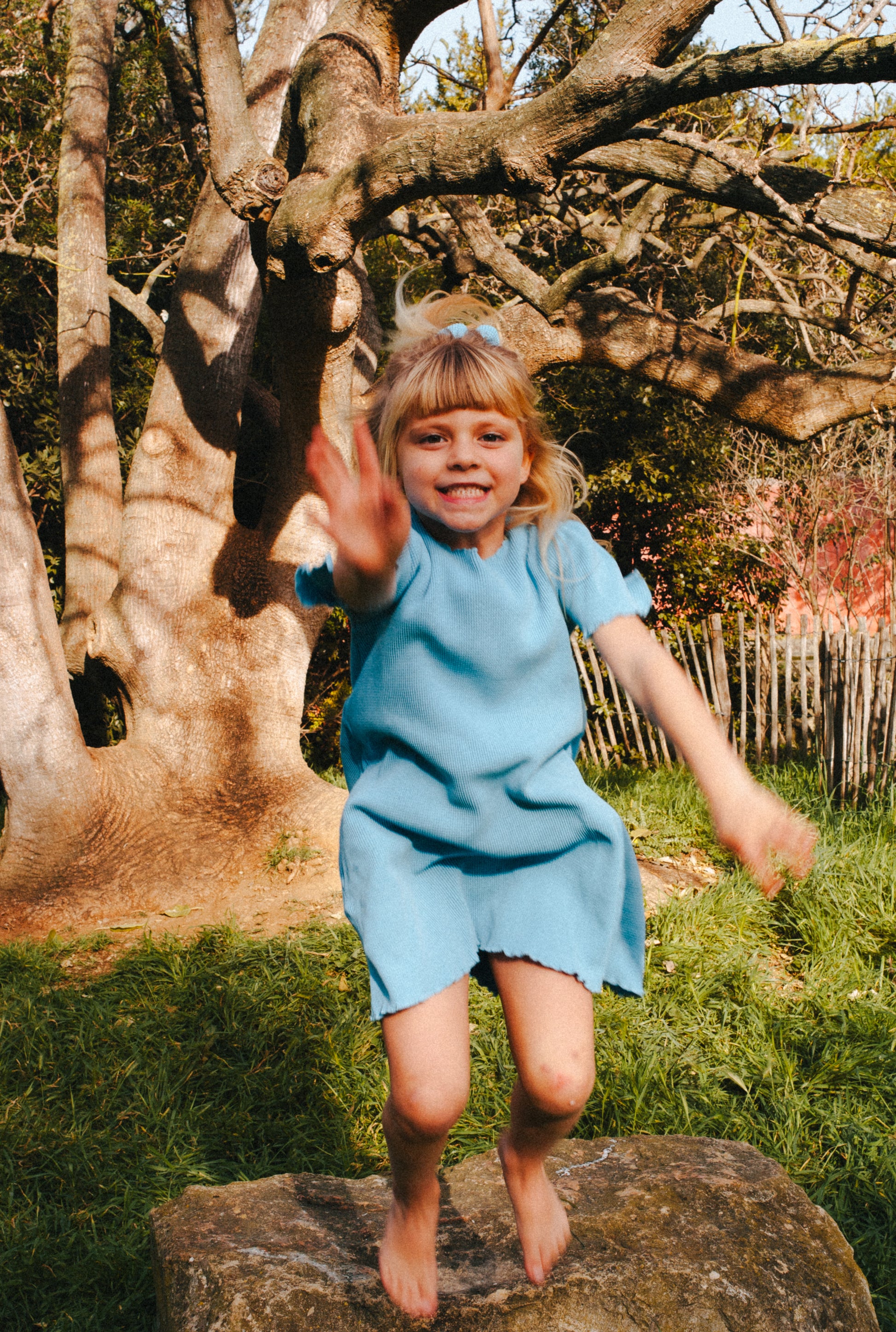 A little girl jumping in the field in the most comfortable blue dress made from 100% organic cotton waffle.