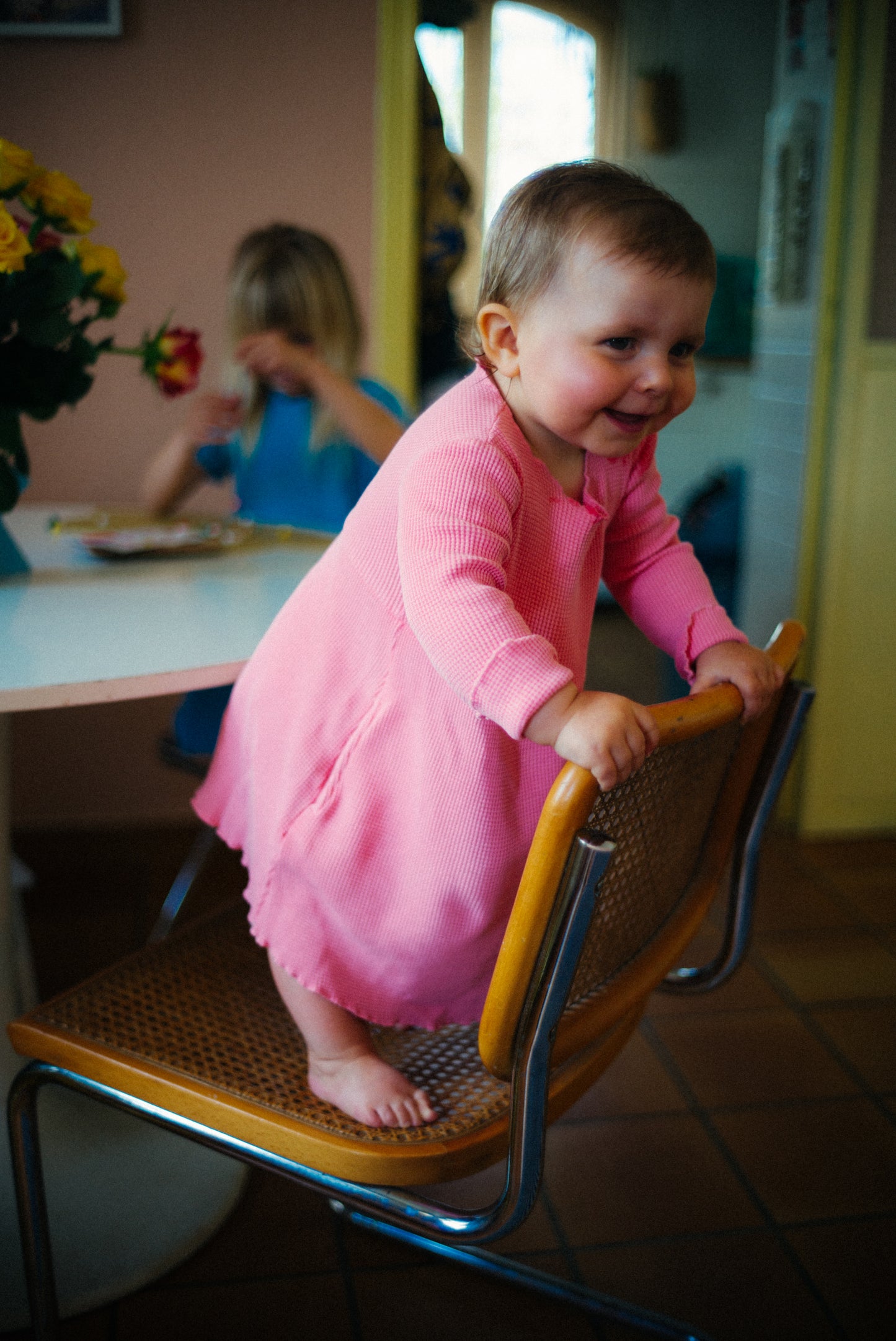 A little girl jumping on the chair in her little cotton dress. The dress is made from 100% organic cotton and garment dyed in natural minerals. It comes with pockets.