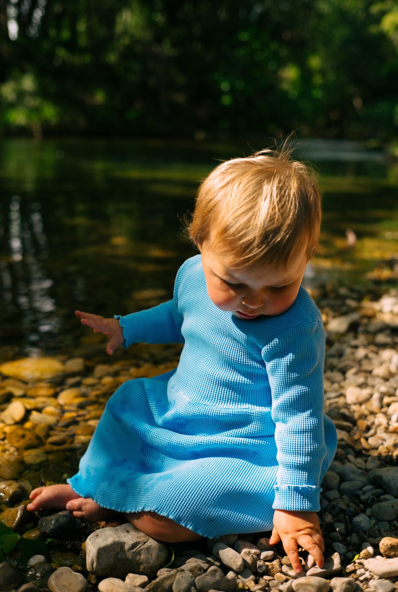 A toddler girl is wearing a long sleeve blue dress by the river in South of France. The dress is long sleeves and comes with lovely pockets. It is comfortable, breathable, and affordable.